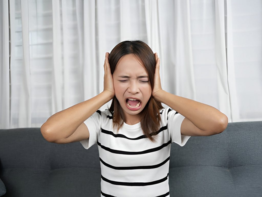 woman sitting by a window, covering her ears
